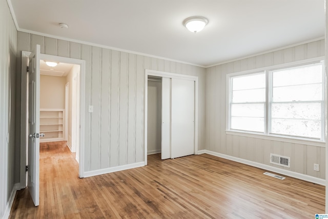 unfurnished bedroom with a closet, light hardwood / wood-style floors, and ornamental molding