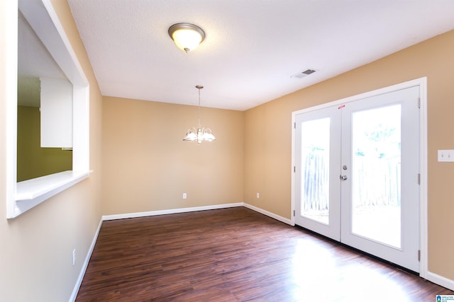 unfurnished room with french doors, a textured ceiling, dark wood-type flooring, and a notable chandelier