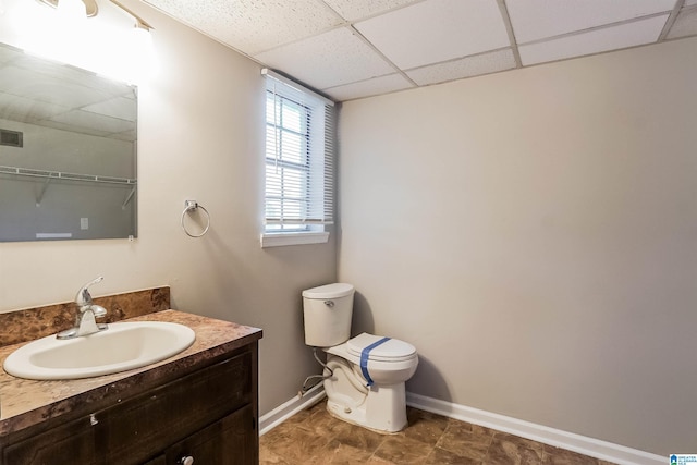 bathroom featuring vanity, toilet, and a drop ceiling