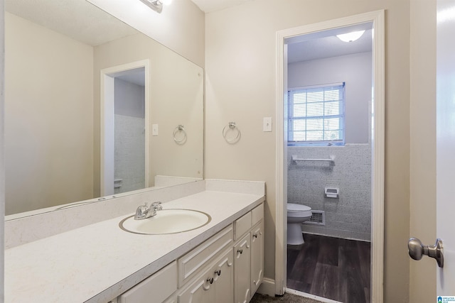 bathroom with toilet, vanity, tile walls, and hardwood / wood-style flooring