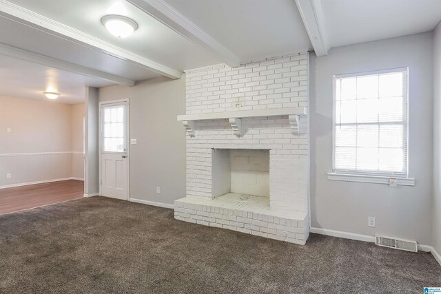 unfurnished living room with dark colored carpet, a brick fireplace, and beamed ceiling