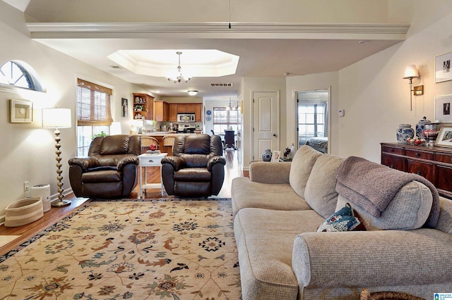 living room with light hardwood / wood-style floors, a raised ceiling, a notable chandelier, and crown molding