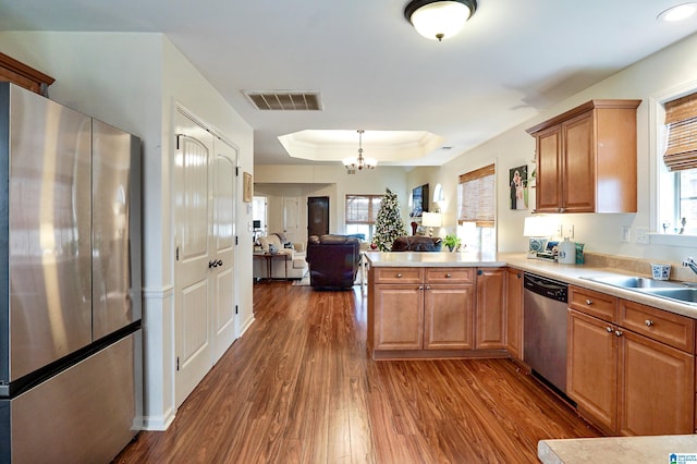 kitchen featuring an inviting chandelier, a raised ceiling, sink, kitchen peninsula, and stainless steel appliances