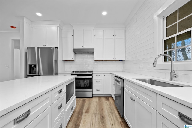 kitchen with appliances with stainless steel finishes, light wood-type flooring, white cabinetry, and sink