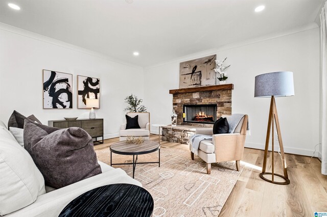 living room with light hardwood / wood-style flooring, a stone fireplace, and crown molding