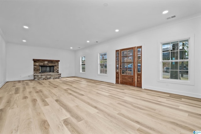 unfurnished living room featuring light hardwood / wood-style floors, a stone fireplace, and crown molding