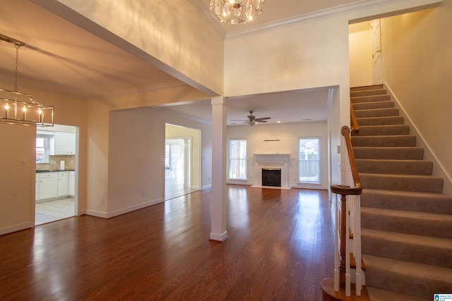 unfurnished living room featuring ornamental molding, ceiling fan with notable chandelier, and hardwood / wood-style flooring