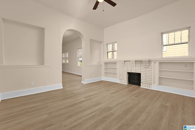 unfurnished living room featuring hardwood / wood-style flooring, ceiling fan, built in features, and a brick fireplace