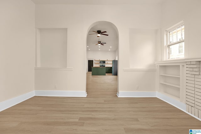 spare room with built in shelves, light hardwood / wood-style flooring, and ceiling fan