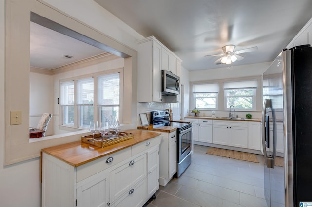 kitchen featuring stainless steel appliances, sink, white cabinets, butcher block countertops, and plenty of natural light