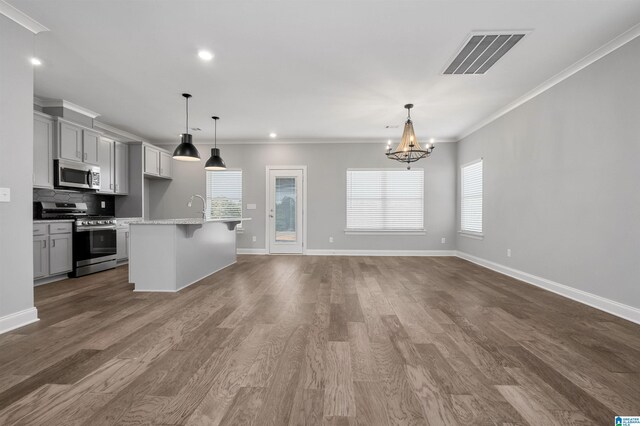 kitchen with ornamental molding, stainless steel appliances, hanging light fixtures, and a center island with sink