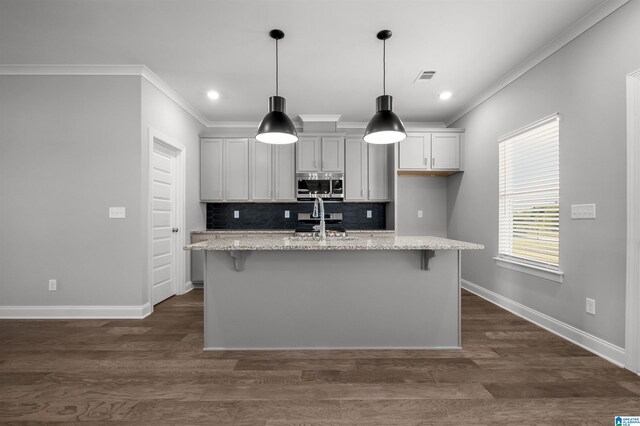 kitchen featuring appliances with stainless steel finishes, light stone counters, a kitchen island with sink, and ornamental molding