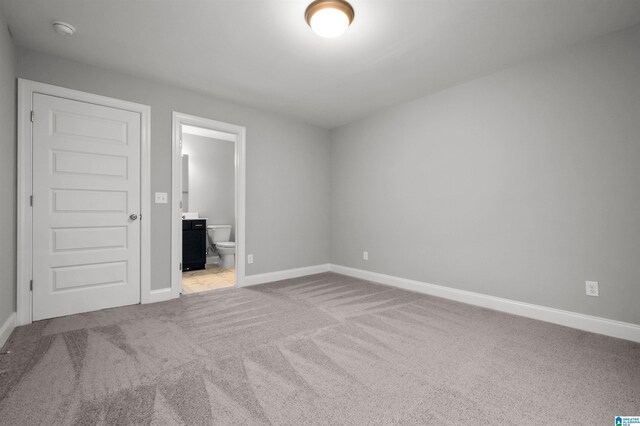 unfurnished bedroom with ensuite bath and light colored carpet