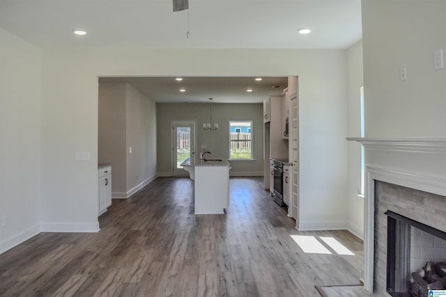 kitchen featuring light stone countertops, wood-type flooring, decorative light fixtures, a kitchen island with sink, and white cabinets