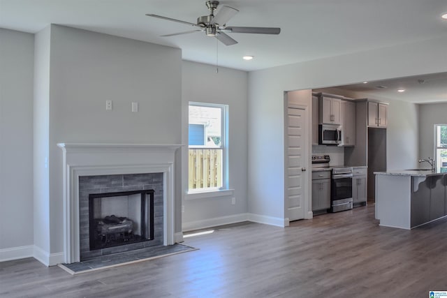 unfurnished living room featuring a tiled fireplace, ceiling fan, dark hardwood / wood-style flooring, and sink