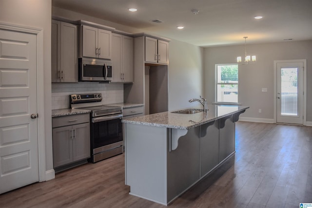 kitchen with a kitchen island with sink, sink, light wood-type flooring, light stone countertops, and stainless steel appliances