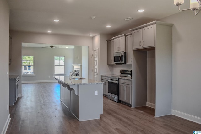 kitchen with a center island with sink, ceiling fan with notable chandelier, a kitchen breakfast bar, sink, and appliances with stainless steel finishes