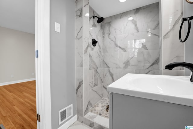 full bathroom with a marble finish shower, visible vents, vanity, wood finished floors, and baseboards