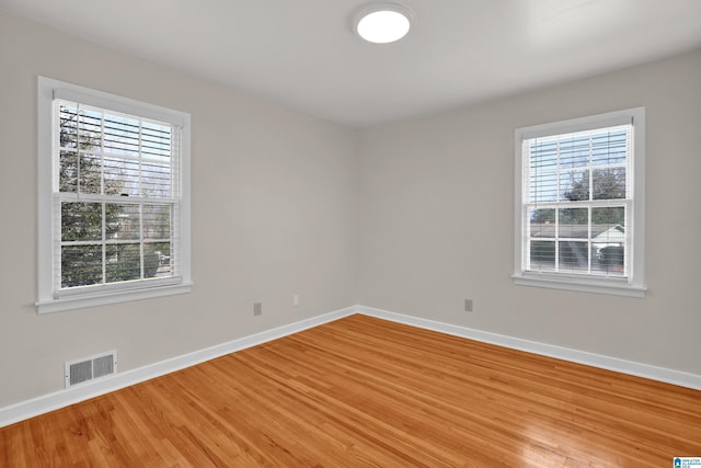 empty room featuring wood finished floors, visible vents, and baseboards