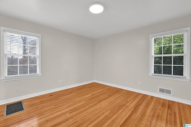 spare room with wood finished floors, visible vents, and baseboards