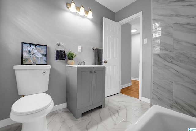 bathroom featuring marble finish floor, toilet, vanity, a tub, and baseboards