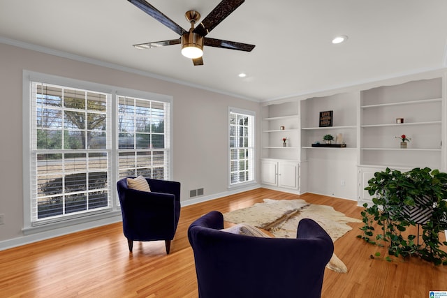 living room featuring built in shelves, light hardwood / wood-style floors, ceiling fan, and crown molding