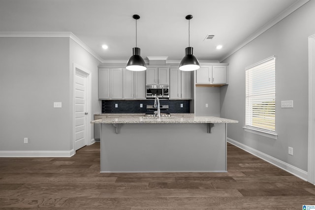 kitchen featuring light stone countertops, an island with sink, ornamental molding, and appliances with stainless steel finishes