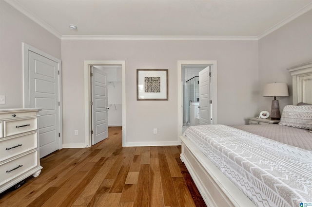 bedroom featuring baseboards, crown molding, a walk in closet, connected bathroom, and wood finished floors