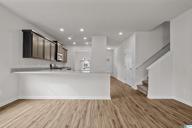 kitchen featuring kitchen peninsula, appliances with stainless steel finishes, light wood-type flooring, light stone counters, and dark brown cabinets