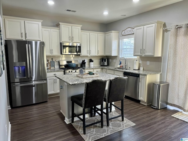 kitchen with white cabinets, sink, appliances with stainless steel finishes, a kitchen island, and light stone counters