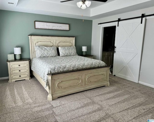 carpeted bedroom featuring a barn door, a raised ceiling, and ceiling fan