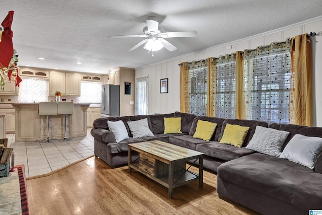 living room with ceiling fan, light hardwood / wood-style floors, ornamental molding, and a textured ceiling