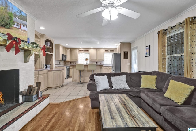 living room featuring crown molding, ceiling fan, light wood-type flooring, a fireplace, and a textured ceiling