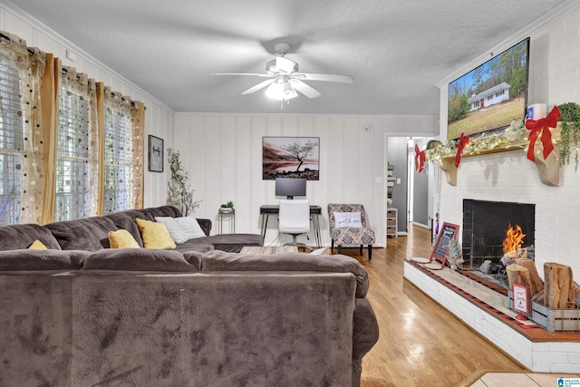 living room with crown molding, hardwood / wood-style flooring, ceiling fan, a fireplace, and a textured ceiling