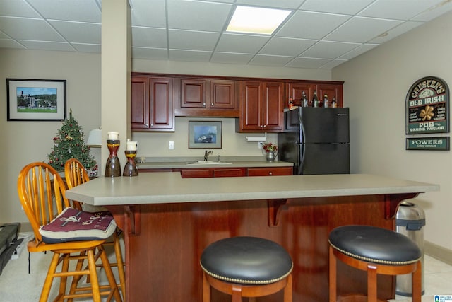 kitchen with a breakfast bar, black refrigerator, a drop ceiling, and sink