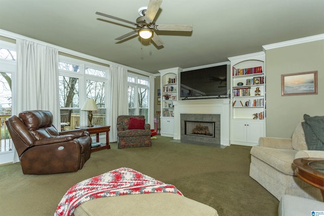 living room with carpet, built in shelves, ceiling fan, crown molding, and a fireplace