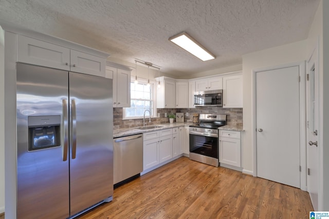 kitchen featuring white cabinetry, sink, stainless steel appliances, decorative light fixtures, and light wood-type flooring