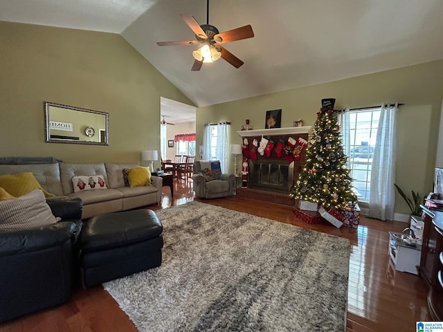 living room with vaulted ceiling, ceiling fan, hardwood / wood-style floors, and a stone fireplace