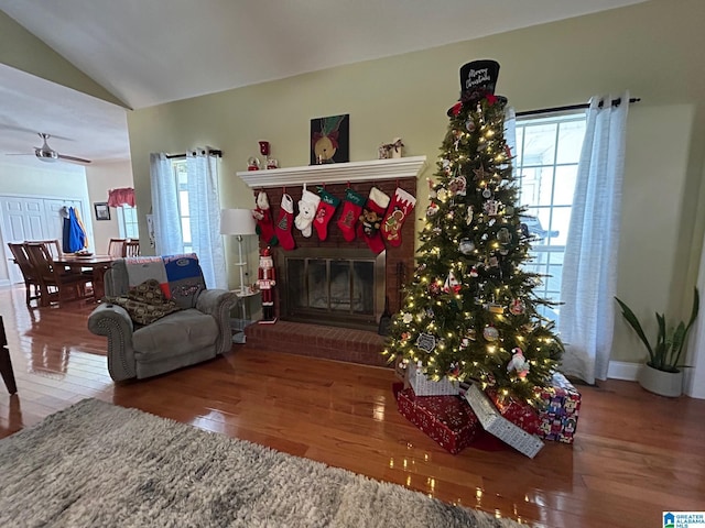 living room featuring hardwood / wood-style flooring, lofted ceiling, a brick fireplace, and ceiling fan