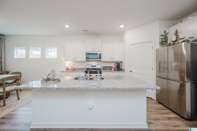 kitchen with stainless steel appliances, white cabinetry, a kitchen island with sink, and light stone counters