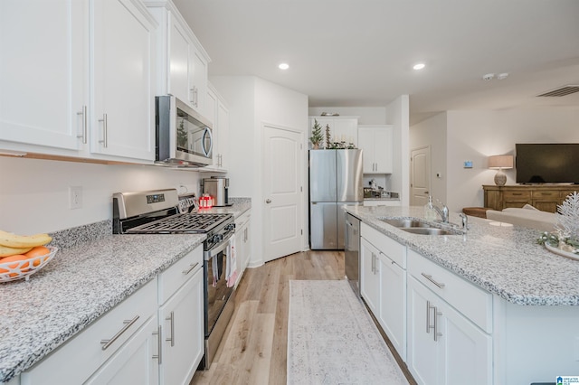 kitchen with light stone countertops, light wood-type flooring, stainless steel appliances, sink, and white cabinetry