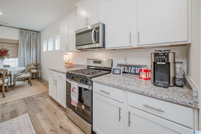 kitchen featuring light stone countertops, white cabinetry, appliances with stainless steel finishes, and light hardwood / wood-style flooring