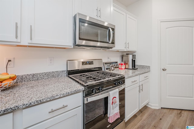 kitchen with white cabinets, light stone counters, light wood-type flooring, and stainless steel appliances