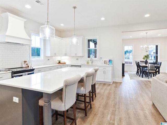 kitchen featuring white cabinetry, a center island, sink, premium range hood, and pendant lighting