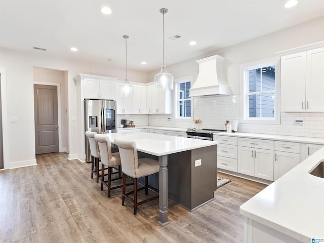 kitchen with white cabinetry, a center island, pendant lighting, custom range hood, and appliances with stainless steel finishes