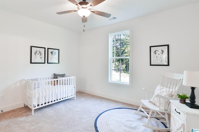 carpeted bedroom featuring ceiling fan and a nursery area