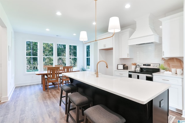 kitchen with white cabinets, stainless steel electric range, a center island with sink, and custom exhaust hood