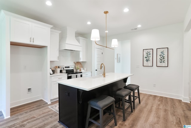 kitchen featuring white cabinetry, sink, a kitchen island with sink, stainless steel range with electric cooktop, and custom range hood