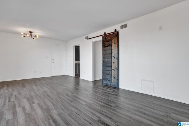 empty room featuring a chandelier, a barn door, and dark wood-type flooring