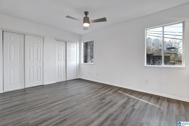 unfurnished bedroom with ceiling fan, dark wood-type flooring, and two closets